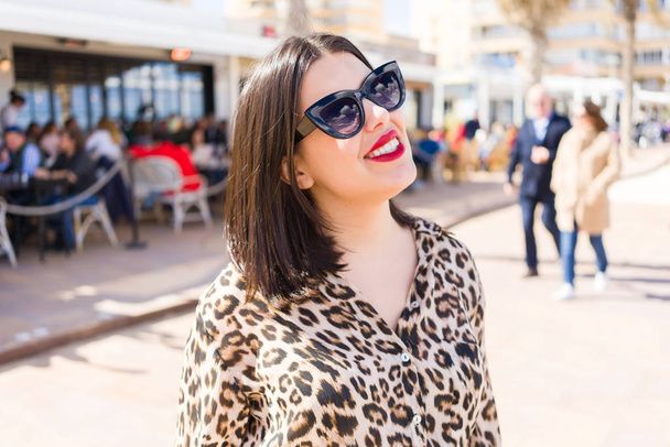 Jeune belle femme aux lèvres rouges portant des lunettes de soleil souriant heureux dans la rue
 - Photo, image