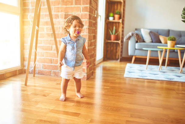 Красивая малышка девочка в синей джинсовой рубашке, стоящей на полу с помощью пустышки
 - Фото, изображение