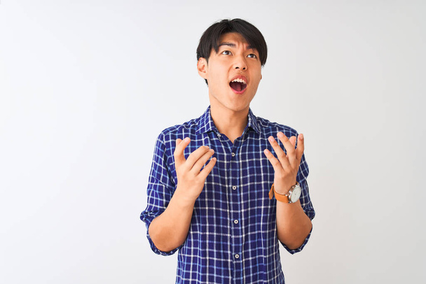 Mladý Číňan v neformální modré košili, stojící nad osamělým bílým pozadím, šíleně křičící a křičící s agresivním výrazem a zdviženýma rukama. Koncept frustrace. - Fotografie, Obrázek