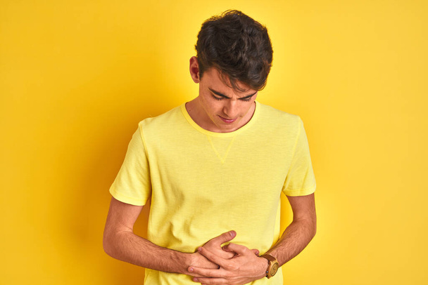 Niño adolescente con camiseta amarilla sobre fondo aislado con la mano en el estómago porque las náuseas, la enfermedad dolorosa sensación de malestar. Concepto Ache
. - Foto, imagen