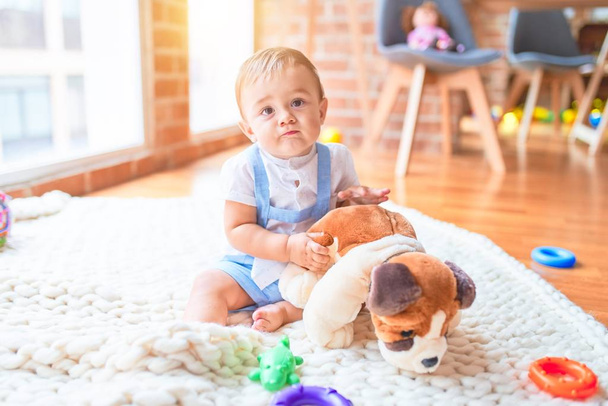 Beau tout-petit assis sur la couverture jouant avec la poupée de chien à la maternelle
 - Photo, image