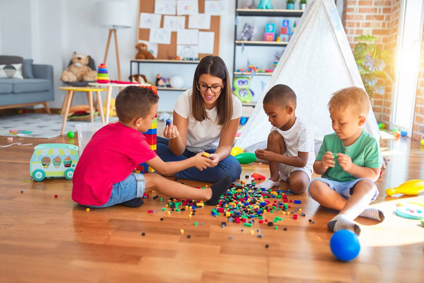 Junge schöne Lehrerin und Kleinkinder spielen im Kindergarten mit Bauklötzen um viele Spielsachen - Foto, Bild