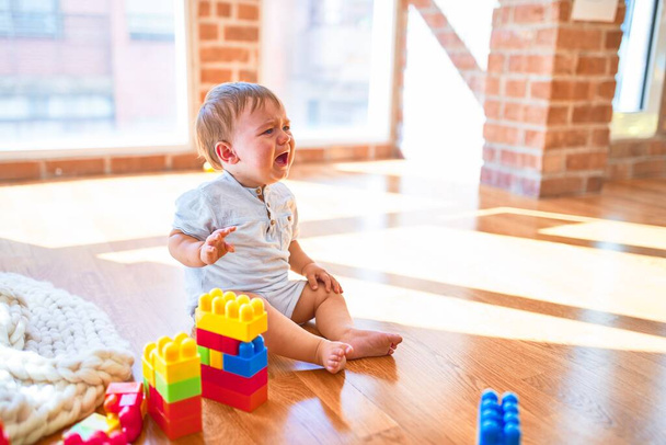 entzückendes Kleinkind sitzt auf dem Boden und weint im Kindergarten um jede Menge Spielzeug - Foto, Bild