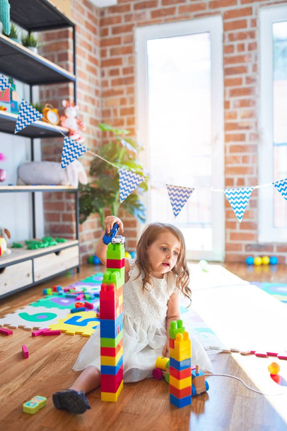 Imádnivaló szőke kisbaba játszik építőkockák körül sok játék óvodában - Fotó, kép