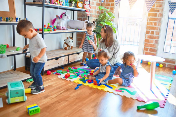 Belo professor e grupo de crianças brincando em torno de lotes de brinquedos no jardim de infância
 - Foto, Imagem