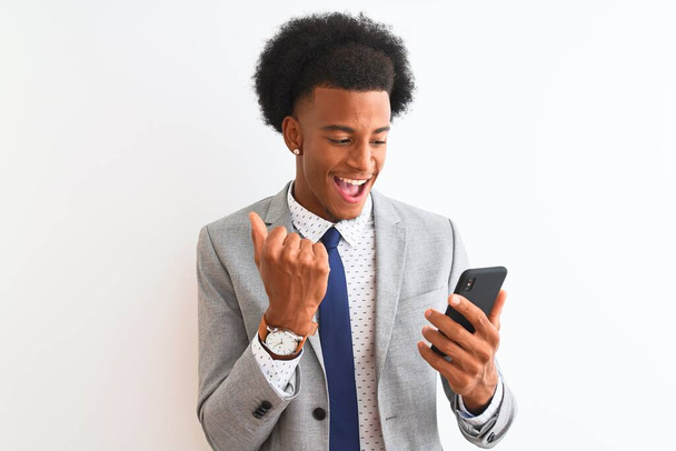 Joven hombre de negocios afroamericano usando smartphone sobre fondo blanco aislado gritando orgulloso y celebrando la victoria y el éxito muy emocionado, animando emoción
 - Foto, Imagen