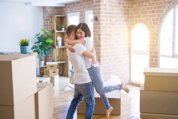 Young beautiful couple hugging at new home around cardboard boxes - Fotografie, Obrázek
