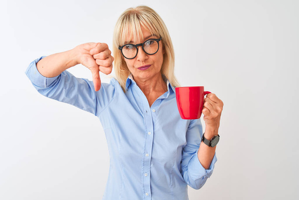 Femme d'affaires d'âge moyen portant des lunettes buvant du café sur fond blanc isolé avec un visage en colère, signe négatif montrant aversion avec les pouces vers le bas, concept de rejet
 - Photo, image