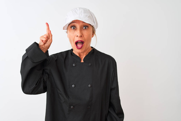 Kochfrau mittleren Alters in Uniform und Mütze steht vor isoliertem weißen Hintergrund und zeigt mit erhobenem Zeigefinger auf eine erfolgreiche Idee. aufgeregt und glücklich. Nummer eins. - Foto, Bild