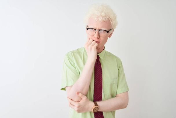 Młody albinos biznesmen noszący koszulę i krawat stojący nad odizolowanym białym tłem wyglądający na zestresowanego i zdenerwowanego rękami obgryzającymi paznokcie. Problem lękowy. - Zdjęcie, obraz