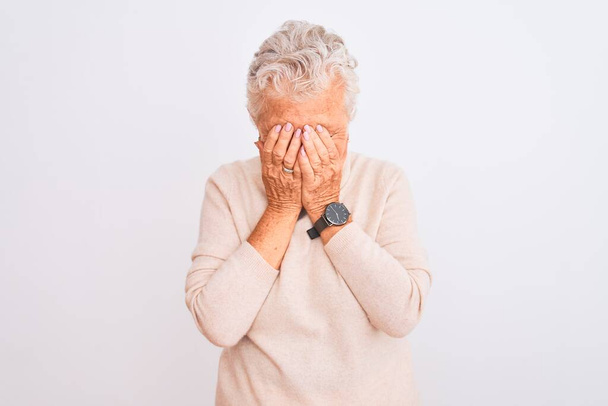 Starsza siwowłosa kobieta w swetrze z golfem stojąca na białym tle ze smutną miną pokrywającą twarz dłońmi podczas płaczu. Koncepcja depresji. - Zdjęcie, obraz