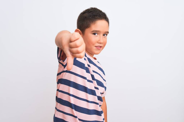 Mooie jongen draagt casual gestreepte t-shirt staan over geïsoleerde witte achtergrond kijken ongelukkig en boos tonen afwijzing en negatief met duimen naar beneden gebaar. Slechte uitdrukking. - Foto, afbeelding