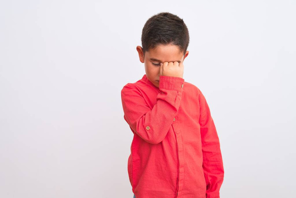 Piękny chłopiec noszący elegancką czerwoną koszulę stojący nad odizolowanym białym tłem zmęczony pocieraniem nosa i oczu uczucie zmęczenia i bólu głowy. Koncepcja stresu i frustracji. - Zdjęcie, obraz