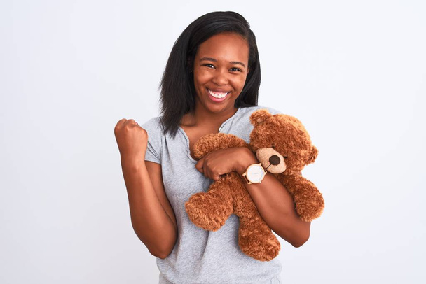 Young african american woman holding teddy bear over isolated background screaming proud and celebrating victory and success very excited, cheering emotion - Фото, зображення