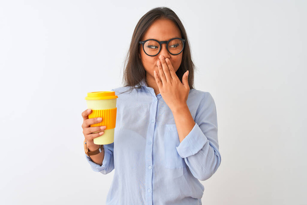 Jeune femme chinoise portant des lunettes tenant un verre de café sur fond blanc isolé couvrir la bouche avec la main choquée par la honte pour erreur, expression de la peur, peur dans le silence, concept secret
 - Photo, image
