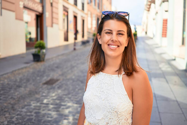 Joven hermosa mujer sonriendo feliz caminando por las calles de la ciudad en un día soleado de verano
 - Foto, Imagen