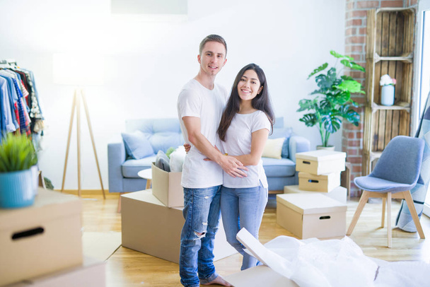 Young beautiful couple hugging at new home around cardboard boxes - Fotoğraf, Görsel
