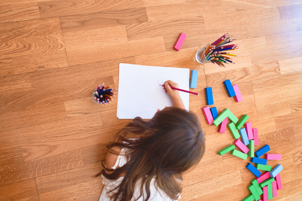 entzückendes Kleinkind, das sich im Kindergarten mit Papier und Bleistift auf den Boden legt - Foto, Bild