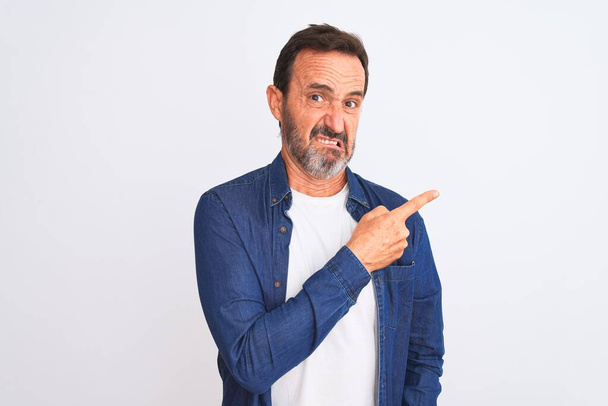 Middle age handsome man wearing blue denim shirt standing over isolated white background Pointing aside worried and nervous with forefinger, concerned and surprised expression - Photo, Image