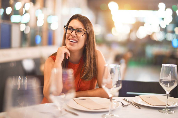 Молодая красивая девушка улыбается счастливой и уверенной, сидя на стуле в ресторане. Отдых с улыбкой на лице
 - Фото, изображение