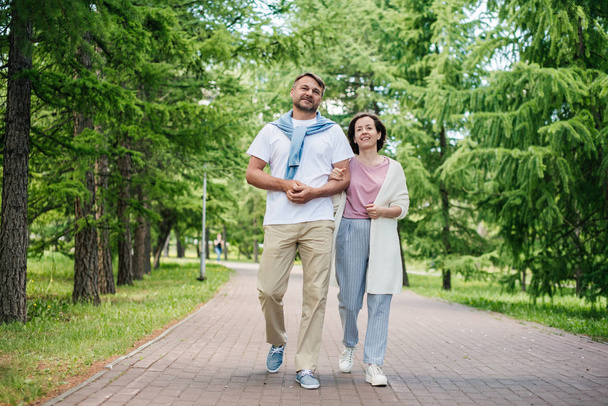 Middle-aged married couple walking in the park smiling. - Foto, afbeelding