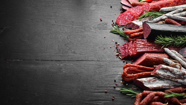 Assortment of sausages, salami and fuet. Dried and smoked salami on black wooden background. Top view. - Foto, Imagem