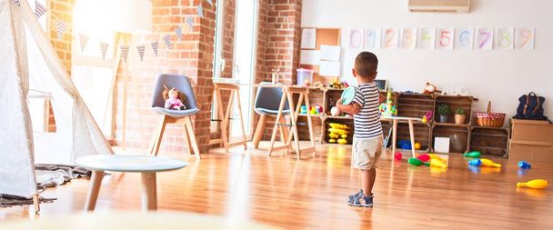 Beautiful toddler boy standing at kindergarten with lots of toys - Photo, Image