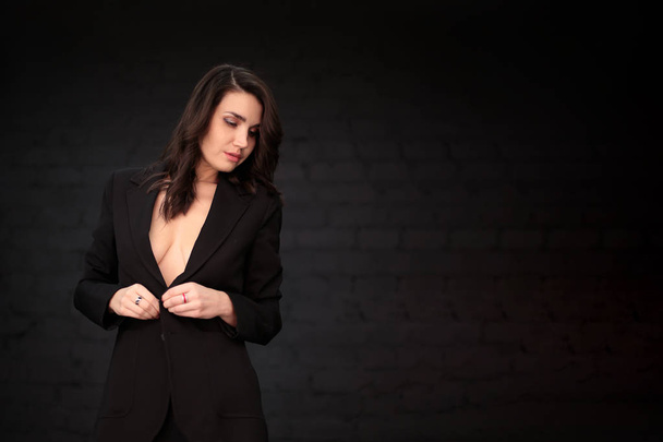 portrait of a beautiful young woman with dark hair in a black man's jacket on a dark background - Photo, image