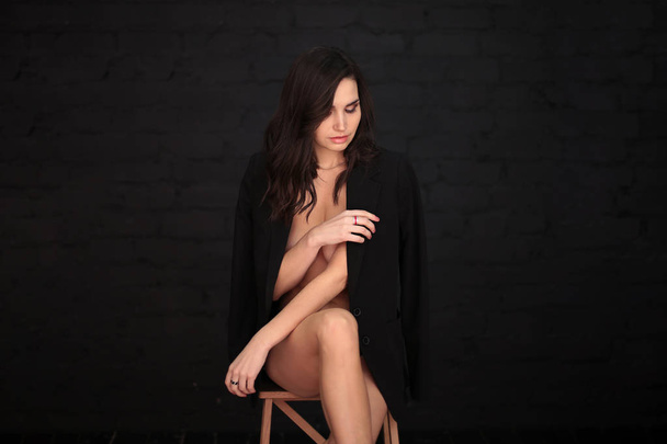 portrait of a beautiful young woman with dark hair in a black man's jacket on a dark background - Photo, image