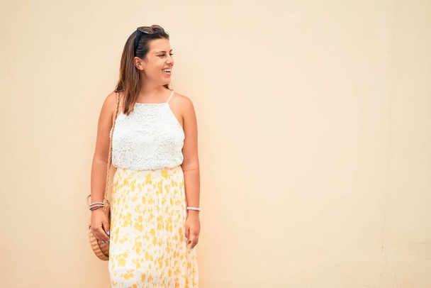 Piękna dziewczyna opierająca się na pomarańczowej ścianie, młoda przyjazna kobieta uśmiechająca się szczęśliwa w słoneczny dzień lata - Zdjęcie, obraz
