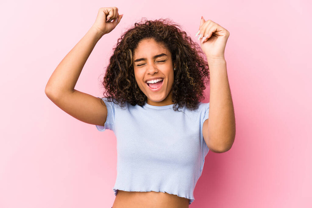 Fiatal afro-amerikai nő rózsaszín háttér ünnepli egy különleges nap, ugrik, és emelje fel a karját az energia. - Fotó, kép