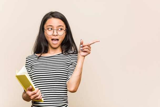 Jeune asiatique femme étudiant tenant un livre pointant vers le côté
 - Photo, image
