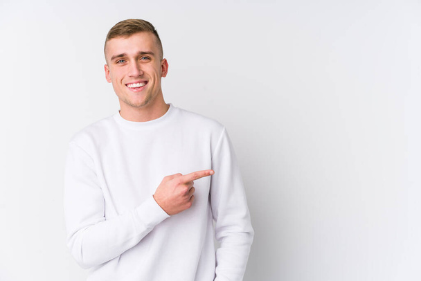 Young caucasian man on white background smiling and pointing aside, showing something at blank space. - Photo, Image