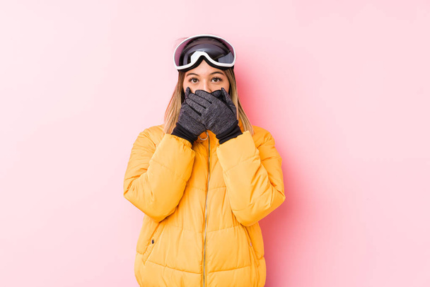 Mujer caucásica joven con una ropa de esquí en un fondo rosa impactado cubriendo la boca con las manos
. - Foto, Imagen