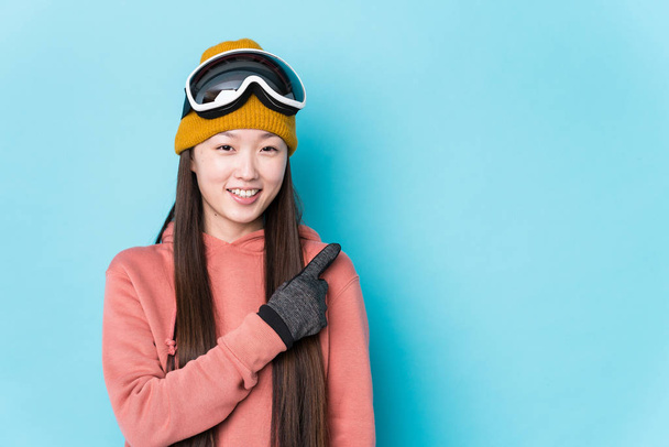 若い中国人女性スキー服を着て孤立笑顔と脇を指して、空白のスペースで何かを示す. - 写真・画像