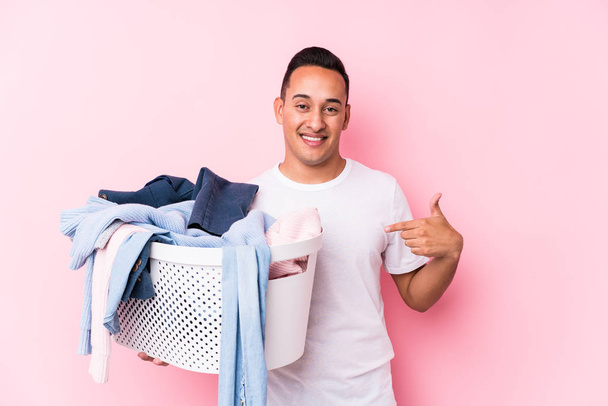 junger lateinischer Mann, der schmutzige Kleidung aufhebt, isolierte Person, die mit der Hand auf einen Hemdkopierraum zeigt, stolz und selbstbewusst - Foto, Bild