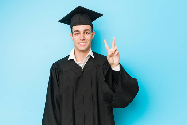 Молодой кавказский выпускник показал номер два пальцами
. - Фото, изображение