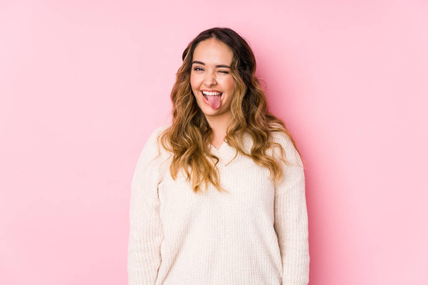 junge kurvige Frau posiert in einem rosa Hintergrund isoliert lustig und freundlich herausstreckende Zunge. - Foto, Bild