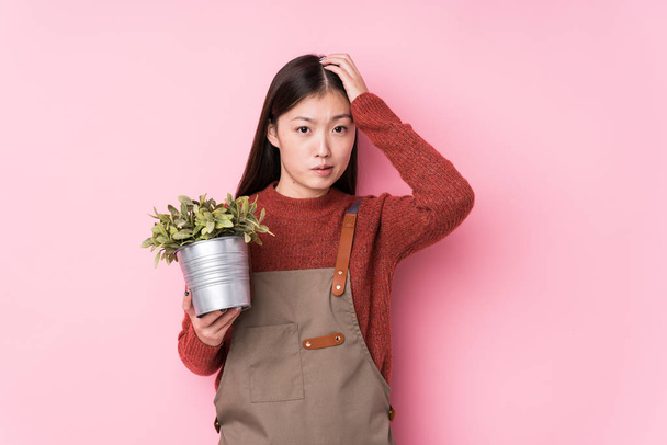 Młoda chińska ogrodniczka trzymająca odizolowaną roślinę w szoku, przypomniała sobie ważne spotkanie. - Zdjęcie, obraz