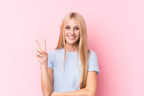 jong blond vrouw op roze achtergrond tonen nummer twee met vingers. - Foto, afbeelding