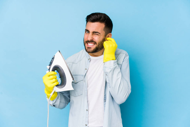 Portrait of young man ironing isolated covering ears with hands. - Foto, Imagen
