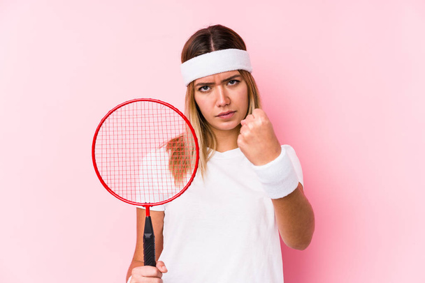 jonge vrouw spelen badminton geïsoleerd tonen vuist naar camera, agressieve gezichtsuitdrukking. - Foto, afbeelding