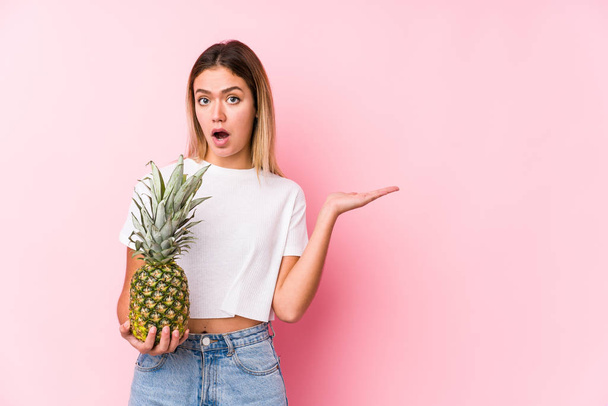 Young caucasian woman holding a pineapple impressed holding copy space on palm. - Photo, Image