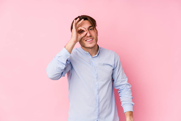 Jovem caucasiano homem posando em um fundo rosa isolado animado mantendo ok gesto no olho
. - Foto, Imagem