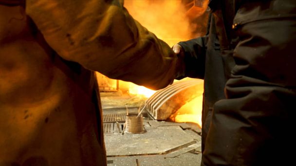 Rear view of two steelmakers at ingot casting shaking hands in front of electric arc furnace in hot shop, metallurgical production. Stock footage. Heavy industry and agreement concept. - Photo, Image