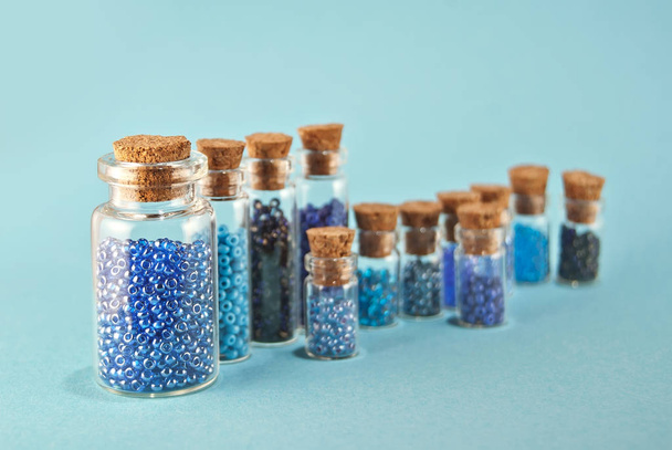 Purple and cyan beads in glass jars on bright blue background. Beads in a transparent container with a wooden cork. The concept of orderliness, balance and chaos. - Valokuva, kuva
