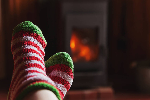 Voeten benen in de winterkleren wollen sokken bij open haard thuis op de winter of herfstavond ontspannen en opwarmen - Foto, afbeelding