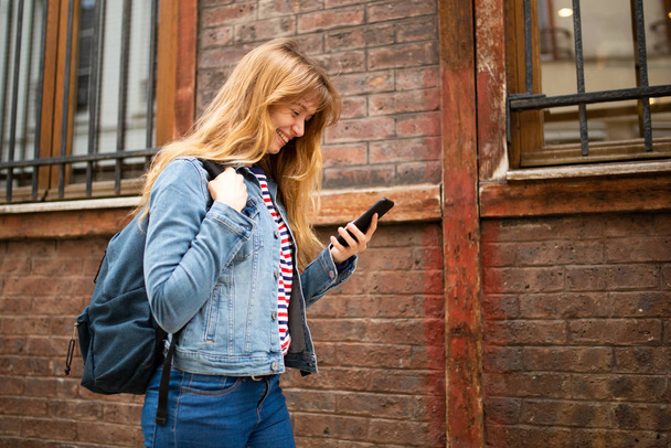 Retrato lateral da jovem caminhando com telefone celular e saco
 - Foto, Imagem