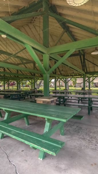 Rama pionowa Wnętrze pawilonu z zielonymi stołami piknikowymi i miejscami siedzącymi w parku w słoneczny dzień - Zdjęcie, obraz