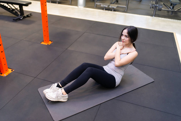 Young fit woman doing sit ups in a gym, six pack free body calisthenic training concept - Foto, afbeelding